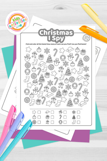 Black and white Christmas I spy Game with festive images for kids to find, such as Christmas trees, ornaments, wreaths, snowmen, stars, Christmas stockings, snowflakes and candy canes; lying on top of a blue-green sheet with multicolored letters on a light brown background.