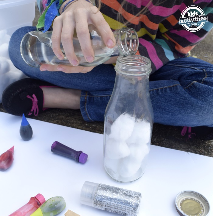 Step 1 - How to make a galaxy jar - bottle 1/2 full of cotton balls with water being poured in by child