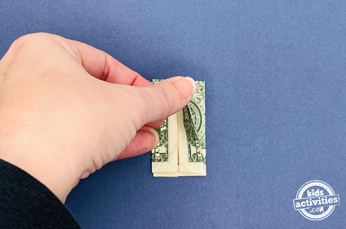 Dollar bill origami pants - Step 7 - Fold the top layer in half, ensuring both sides are symmetrical. Flip the figure and repeat this fold on the other side.