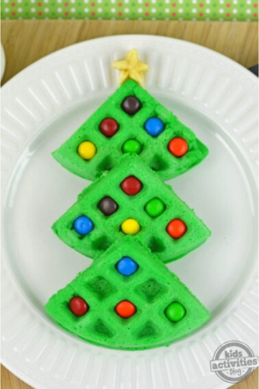 Homemade Merry Christmas Tree Waffles Recipe - Green wafffles, formed in the shape of a Christmas tree, with colorful candies as ornaments, and a small piece of banana cut into a star for the top - Kids Activities Blog