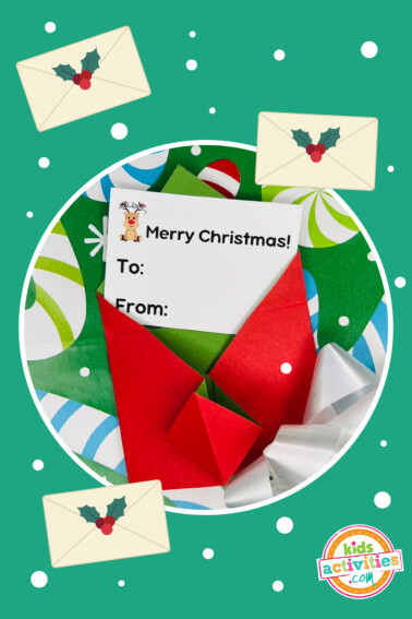 Image shows a DIY origami envelope craft with a Merry Christmas note inside and Christmas decorations outside. Kids Activities Blog