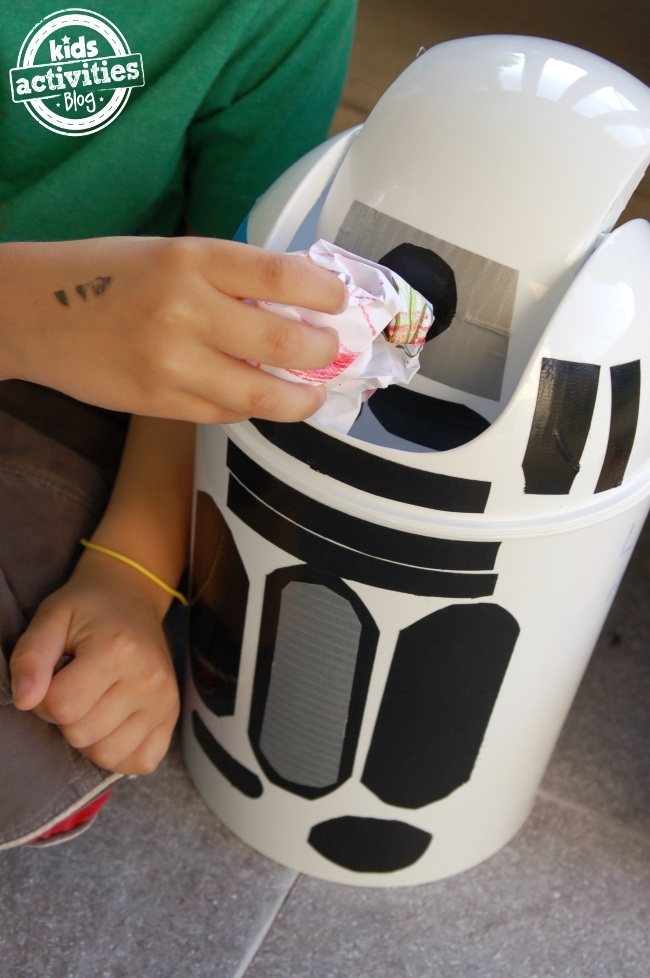 R2D2 Trash Can with child holding paper wad placing it into the trash can - Kids Activities Blog