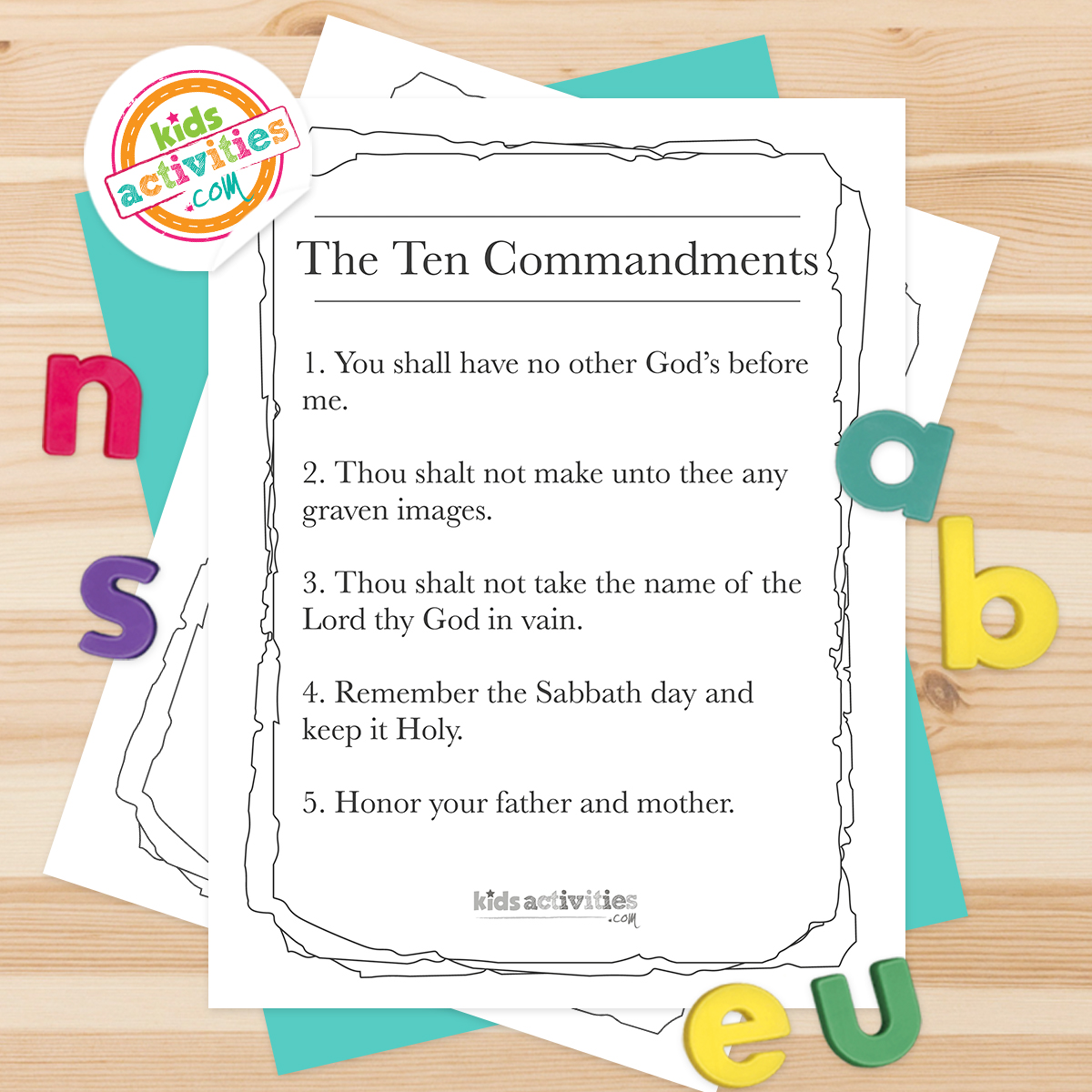 Black and white coloring pages with The Ten Commandments lying on top of blue-green sheets with assorted letters on a light wooden background.